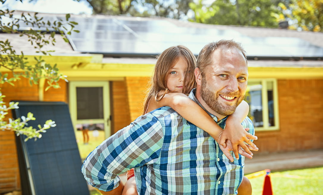 A man and a young girl standing in front of a house with solar panels on the roof